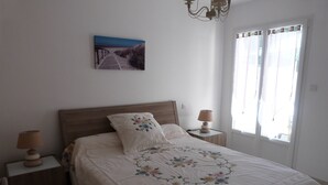 Un dormitorio con cabecera de madera, colcha con estampado floral, dos lámparas de noche, una mesita de noche y una ventana con cortinas.
