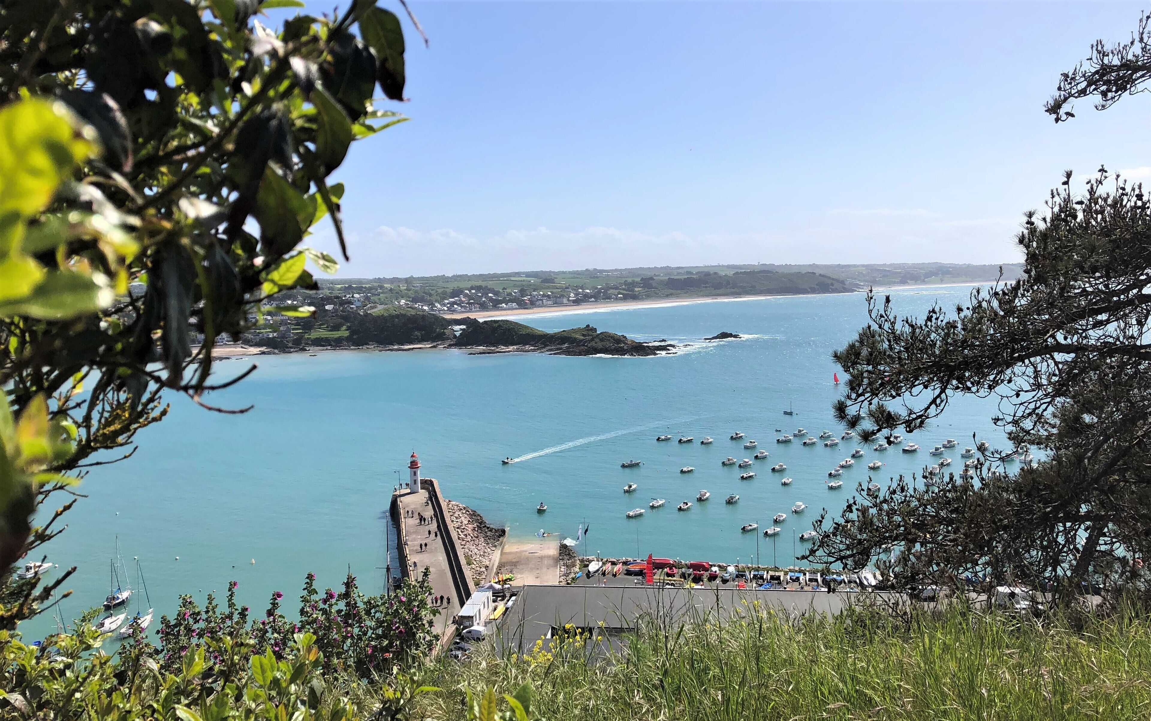 A coastal view with a lighthouse, boats, and a pier.