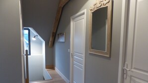 Ein schmaler Korridor mit Holzdielen, weißen Türen und einem Spiegel an der Wand.