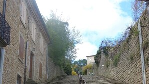 Una escalera de piedra que asciende por una colina, bordeada por edificios con paredes de piedra y contraventanas de madera.