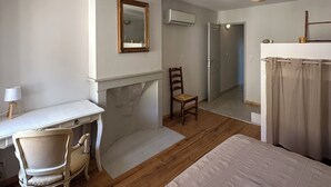 Un dormitorio con cama, escritorio, silla, espejo y aire acondicionado.