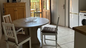 Una cocina con una mesa redonda de comedor, dos sillas, un armario de madera, un refrigerador y una lavadora.