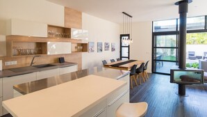 Cozinha moderna com ilha central, área de refeições com mesa grande e cadeiras, e uma janela ampla com vista para o exterior.