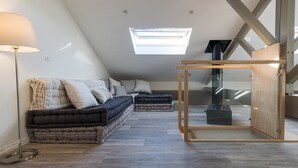Quarto em estilo loft com claraboia, sofá-cama, aquecedor vertical e armário de madeira.