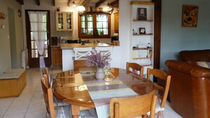 A dining area with a wooden table, chairs, and a vase of flowers. There is a kitchen in the background with wooden cabinets and a window. - La Bouée Rouge: Pool, Ocean, & Lake by Bike, 6 people (Vielle-Saint-Girons)