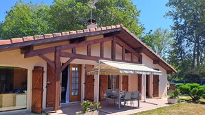 A two-story building with a covered patio area, wooden beams, and a small garden with potted plants. - La Bouée Rouge: Pool, Ocean, & Lake by Bike, 6 people (Vielle-Saint-Girons)