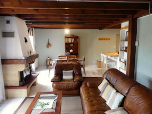 A cozy living room with a brown leather sofa, a dining table, and a bookshelf.