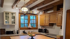 A kitchen with wooden cabinets, a large island with a bowl of fruit, white chairs, and a window with curtains. - La Bouée Rouge: Pool, Ocean, & Lake by Bike, 6 people (Vielle-Saint-Girons)