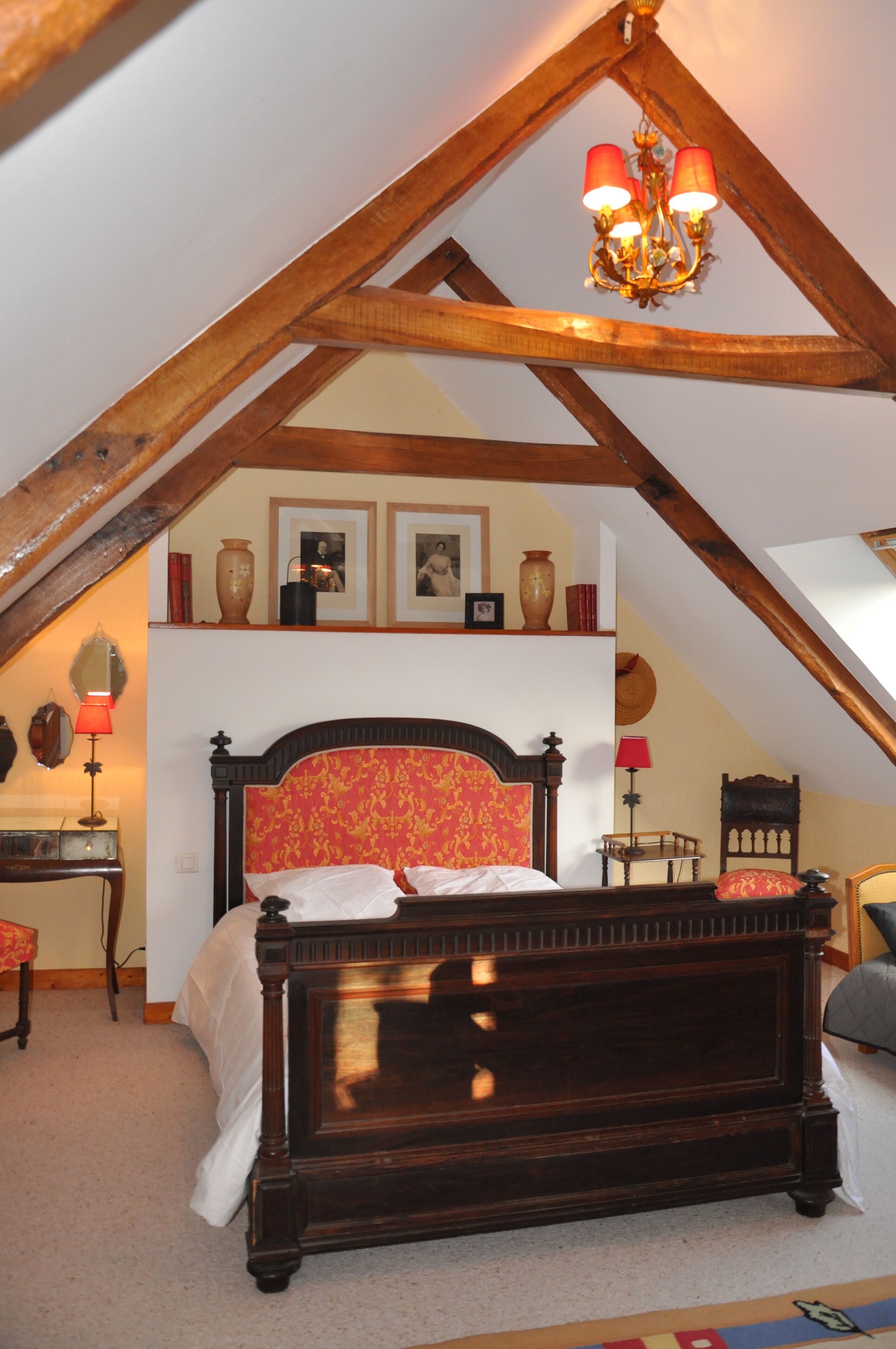 Een slaapkamer met een houten plafond, een bed met een rode hoofdbord en een kroonluchter.