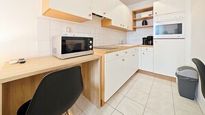 Una cucina moderna con mobili bianchi, forno a microonde integrato, macchina del caffè e cestino.