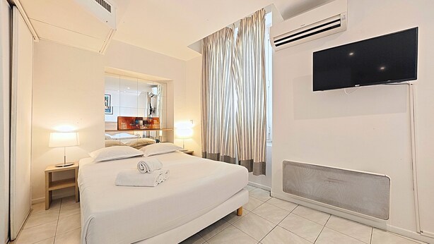 Una camera d'albergo con un letto grande, lampade sui comodini, una TV a schermo piatto, un condizionatore d'aria e una finestra con tende a righe.