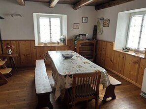A dining area with a long table covered in a floral tablecloth, wooden benches, and a wooden cabinet with shelves. - COSY AND SPACIOUS FARMHOUSE, ALL INCLUSIVE, SLEEPS 9 (Étueffont)