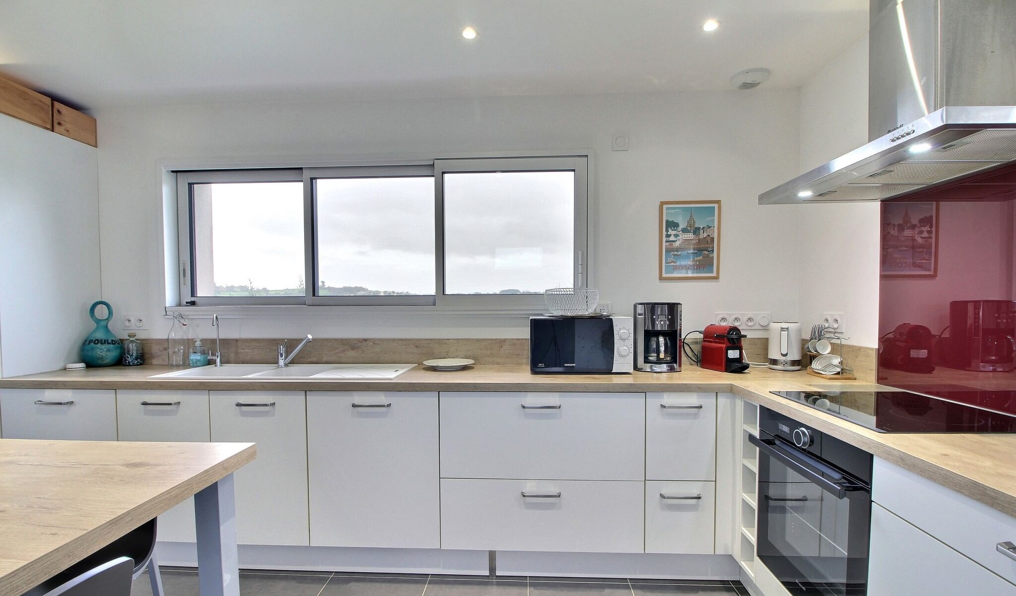 A modern kitchen with white cabinetry, a large window, and a built-in oven.