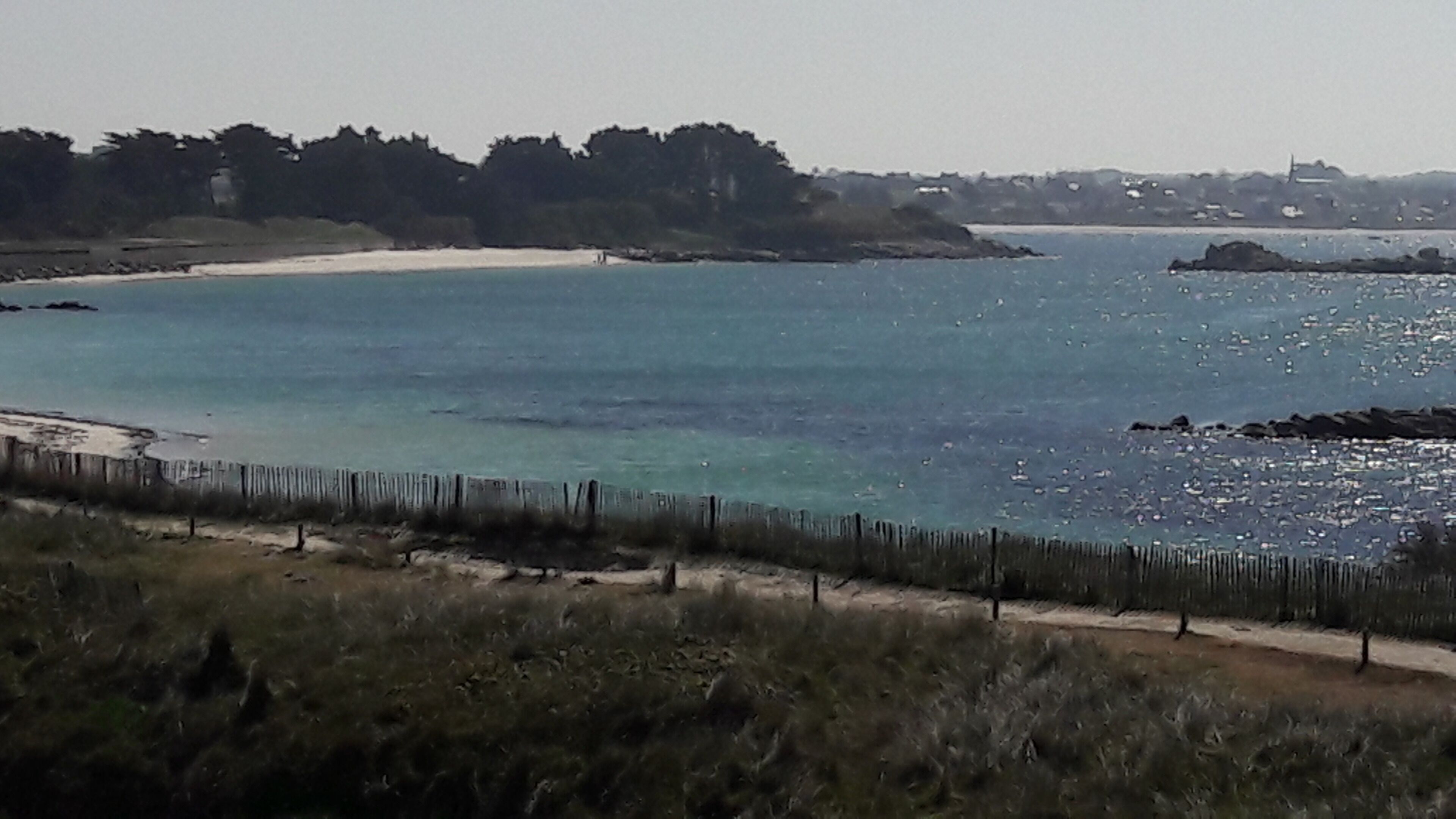 A coastal landscape with a sandy beach, a wooden fence, and a calm sea.
