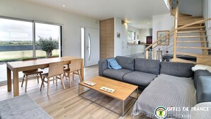 A modern living room with a dining area, a sofa, a coffee table, and a staircase leading to an upper level.