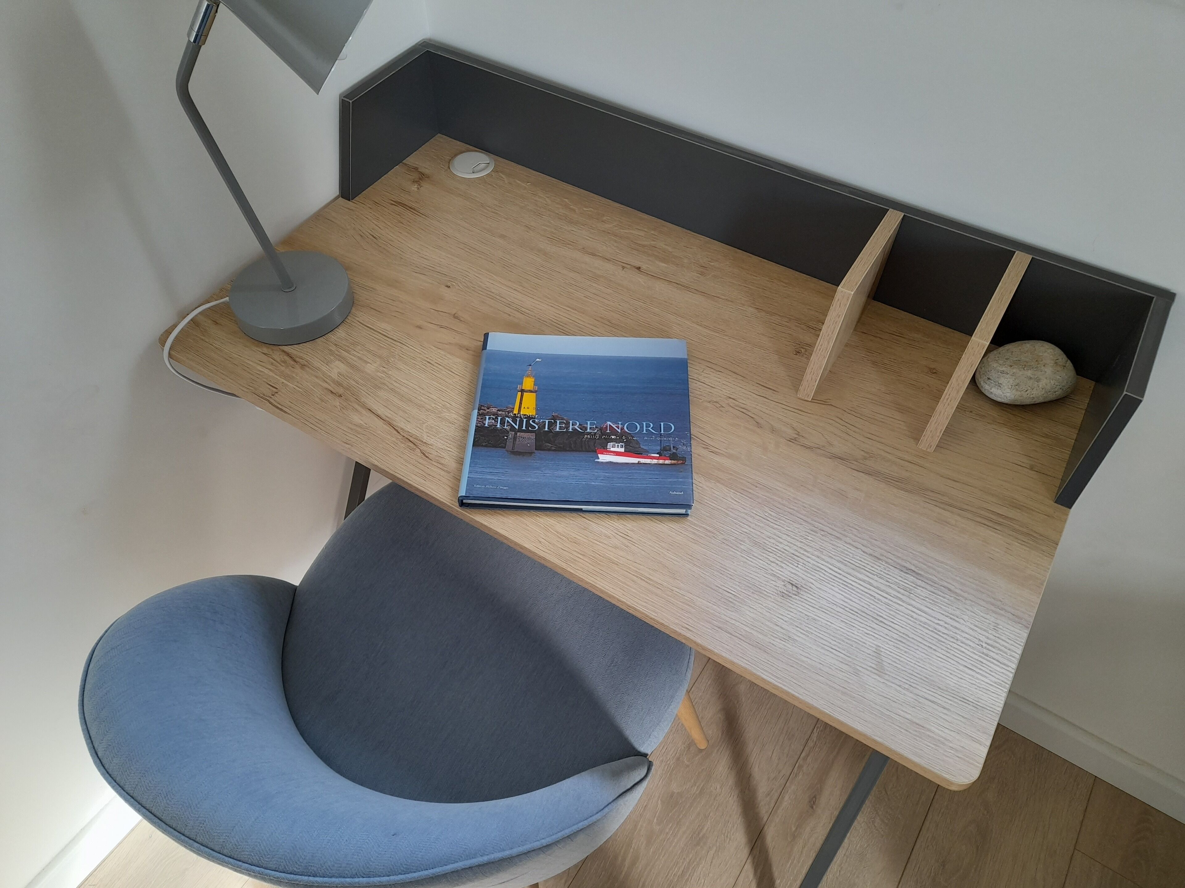 A modern workspace with a wooden desk, a blue chair, and a book titled "FINISTERE NORD".