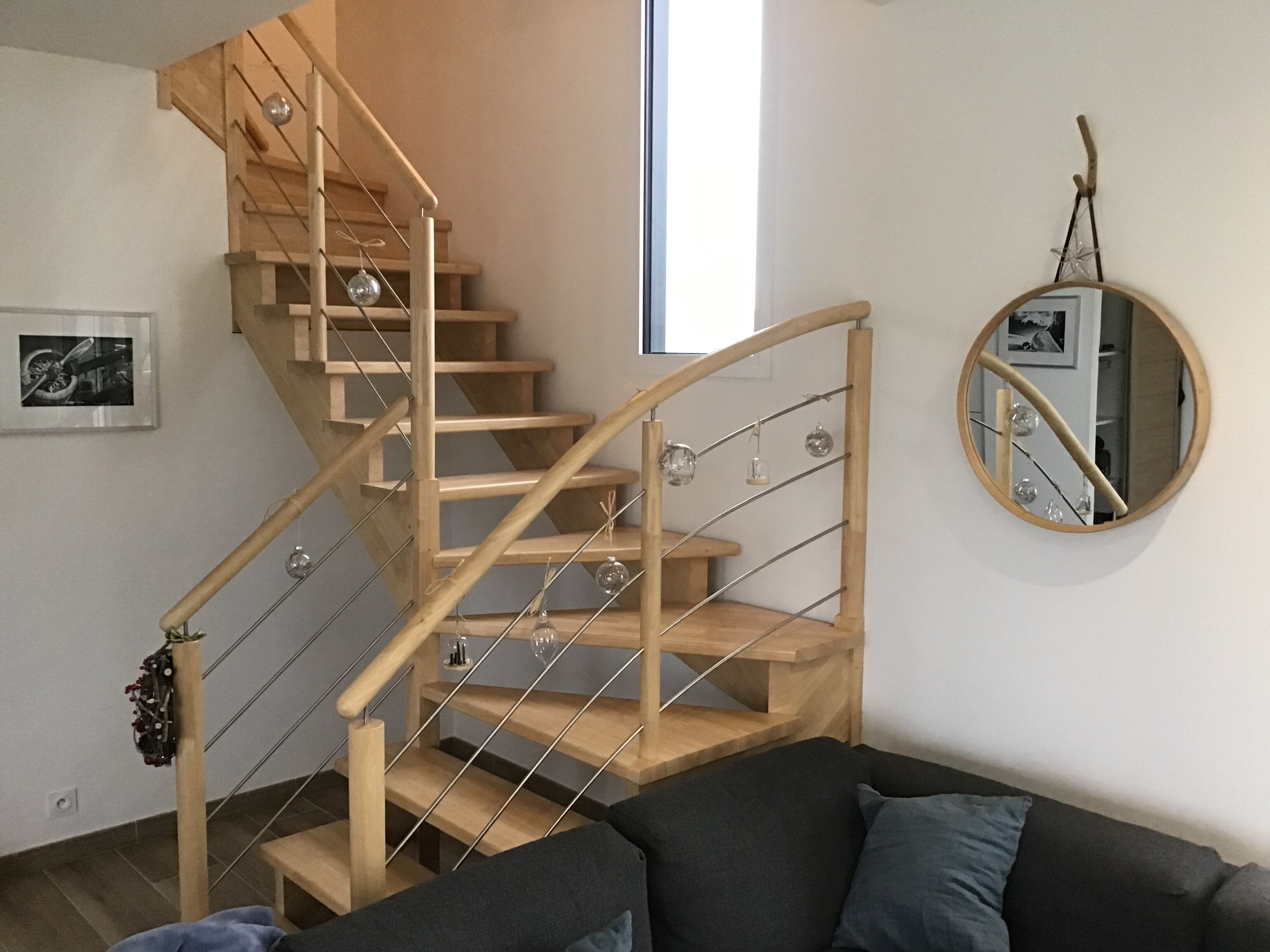 A modern interior with a wooden staircase, a round mirror, and a dark-colored sofa.