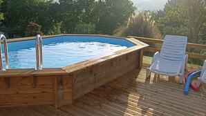 A wooden deck with a hot tub and two white plastic chairs.
