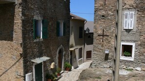 A narrow stone pathway leading to a rustic building with multiple windows and doors, some with shutters.