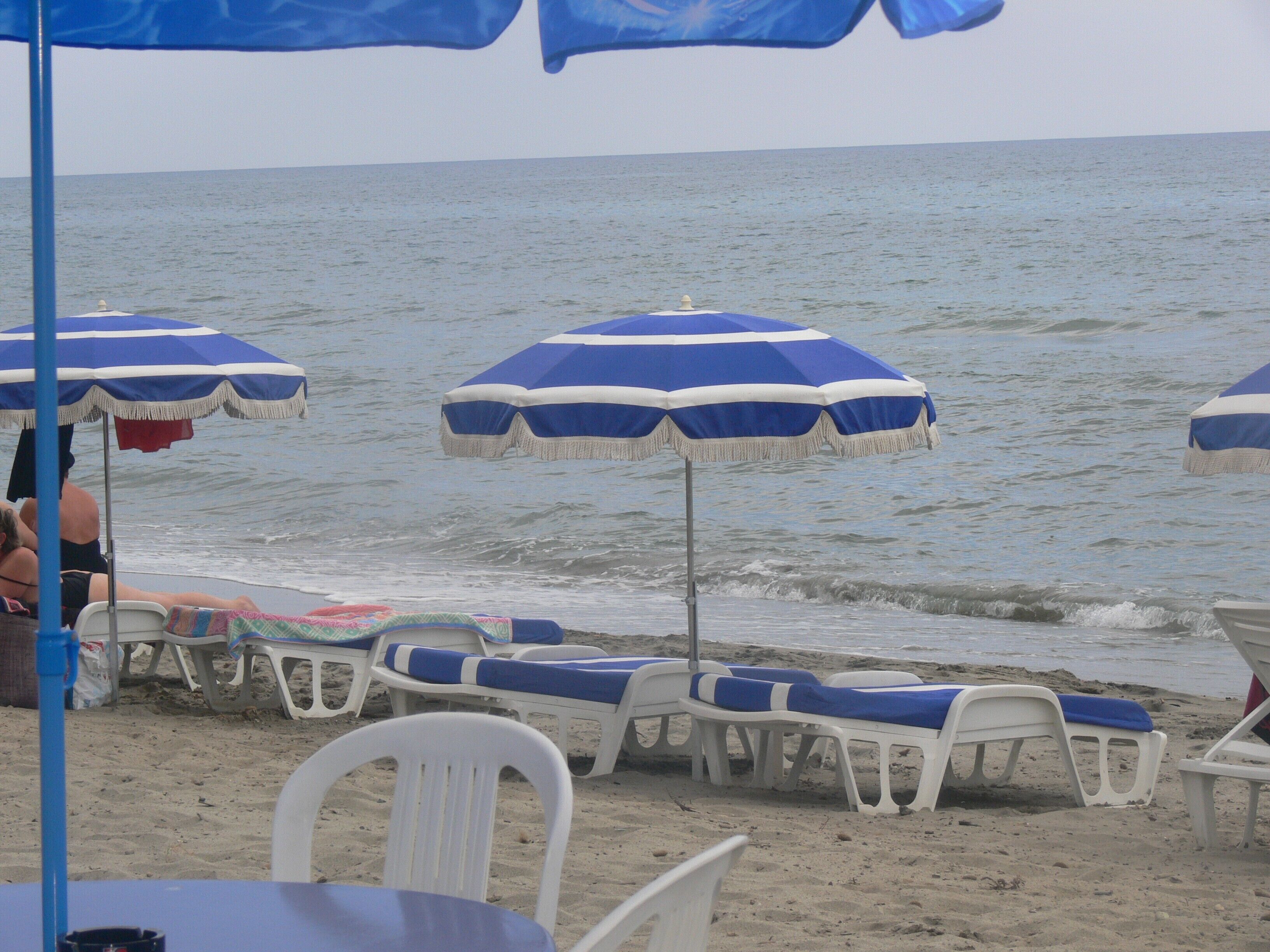 A beach with white lounge chairs and blue umbrellas.