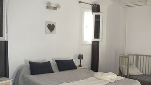 A bedroom with a bed, a nightstand, a lamp, a crib, and a window.