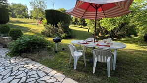 A patio with a table and chairs, a grill, and a striped umbrella.