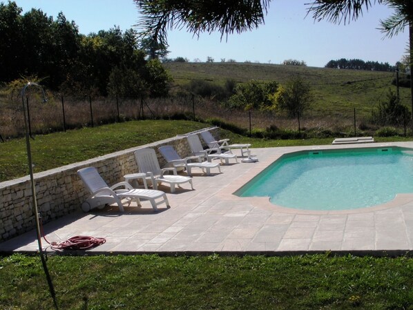 Una piscina con sillas de descanso blancas y un muro de piedra.
