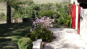 A stone pathway leading to a building with a red door, surrounded by lush greenery and flowering plants.