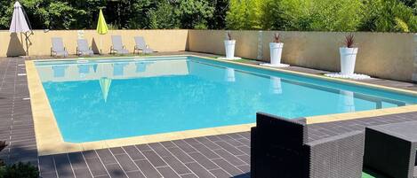 Une piscine rectangulaire, bordée d’une terrasse carrelée, entourée de chaises longues et de plantes en pot.