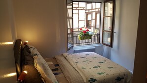 A small, cozy bedroom with a single bed, a nightstand, and a window with a view of a balcony with plants. - L'EUROSEBASTOPOL - Crossing apartment  (Strasbourg)
