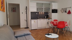 A compact living space with a kitchenette, a dining area with red chairs, a sofa, and a small round table. - L'EUROSEBASTOPOL - Crossing apartment  (Strasbourg)