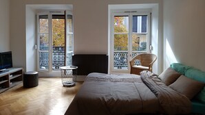 A bedroom with a bed, a chair, a TV, and a radiator. - L'EUROSEBASTOPOL - Crossing apartment  (Strasbourg)