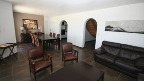 En rummelig opholdsstue med en mørkebrun lædersofa, et spisebord med stole og et sofabord. Et maleri hænger på væggen, og en trappe fører op til et andet niveau.