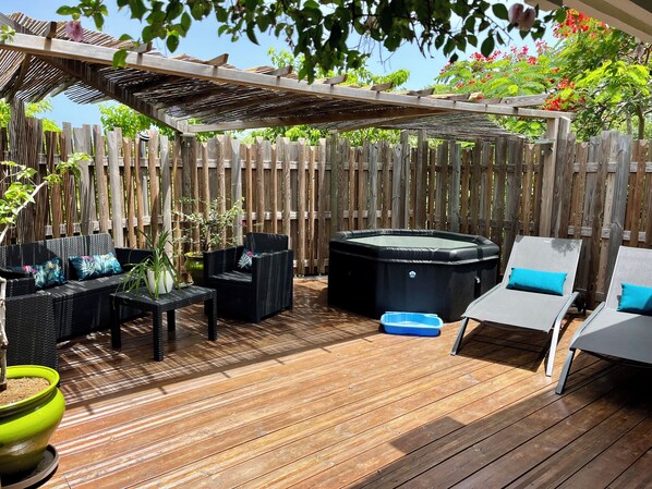 Une terrasse en bois aménagée avec du mobilier d’extérieur, notamment un canapé, des fauteuils et un jacuzzi.