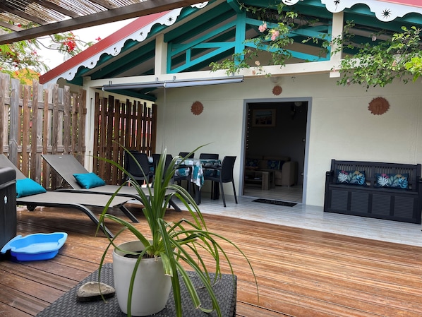 Um deck de madeira com cadeiras de descanso, uma mesa de jantar e um vaso com planta.