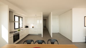 A modern kitchen with white cabinets, a dining area with a wooden table, and a hallway leading to another room. - Superb new apartment "feet in the water" exceptional view on the beach (Mauguio)