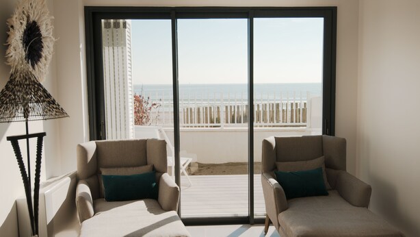 A balcony with two beige armchairs and a floor lamp, overlooking a beach and a white fence. - Superb new apartment "feet in the water" exceptional view on the beach (Mauguio)