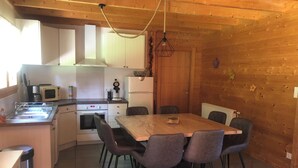 Een kleine keuken met een eethoek, houten wanden en voorzieningen zoals een magnetron, fornuis en spoelbak.