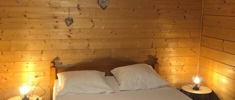 A wooden-paneled bedroom with a bed, two bedside tables with lamps, and heart-shaped wall decorations.