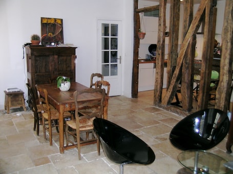 A dining area with a wooden table, chairs, and a glass-top table. There is a cabinet with a plant on top and a door leading to another room.