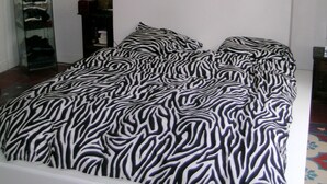 A bed with a zebra print bedspread in a room with a sloped ceiling and a glass cabinet with clothes.