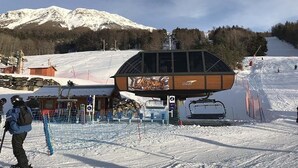 A ski lift station with a wooden cabin, a ski lift, and a snowy mountain backdrop.