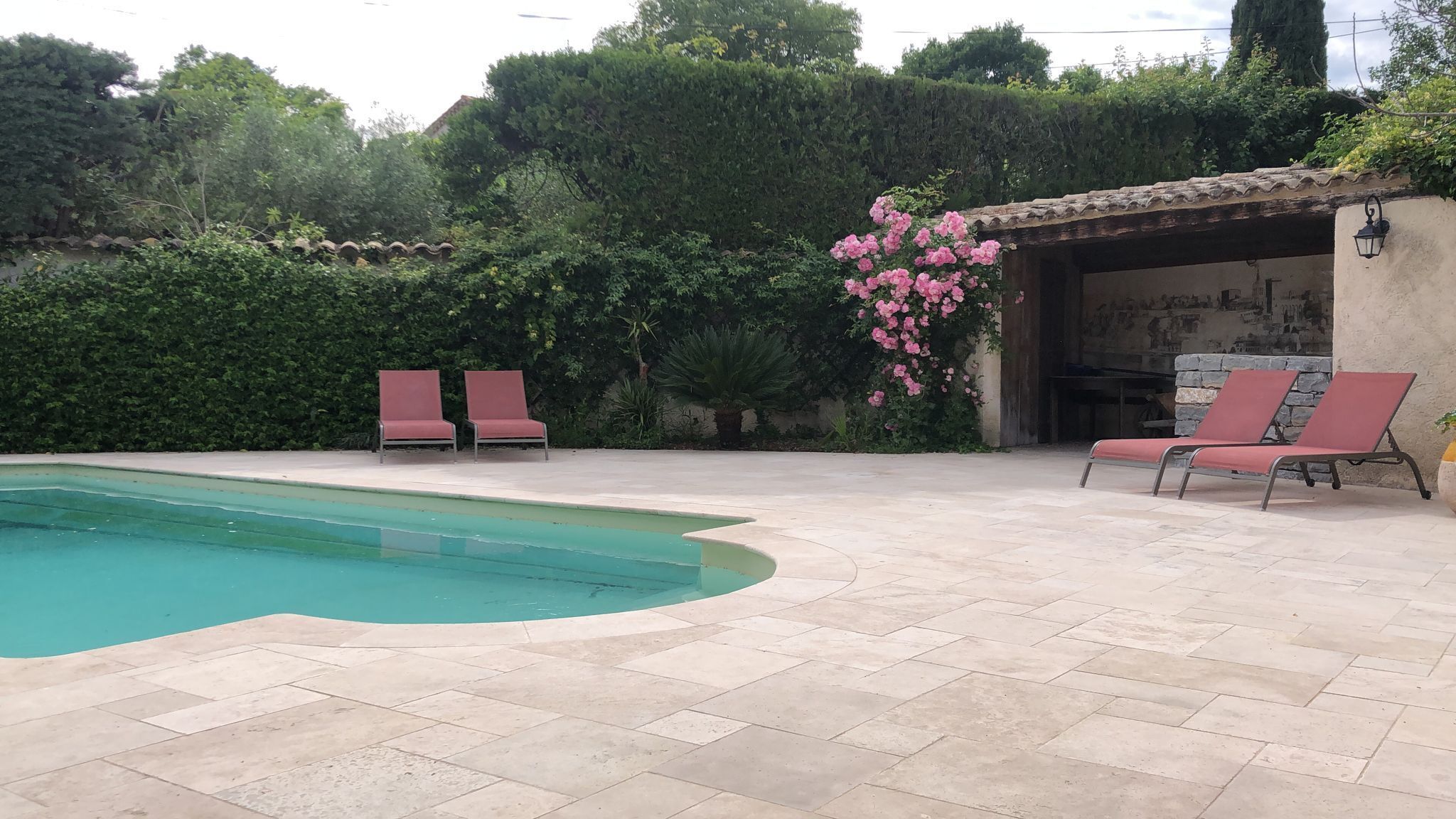 Ein Schwimmbecken mit zwei Liegestühlen und einem Pergola, das mit rosa Blüten bepflanzt ist.