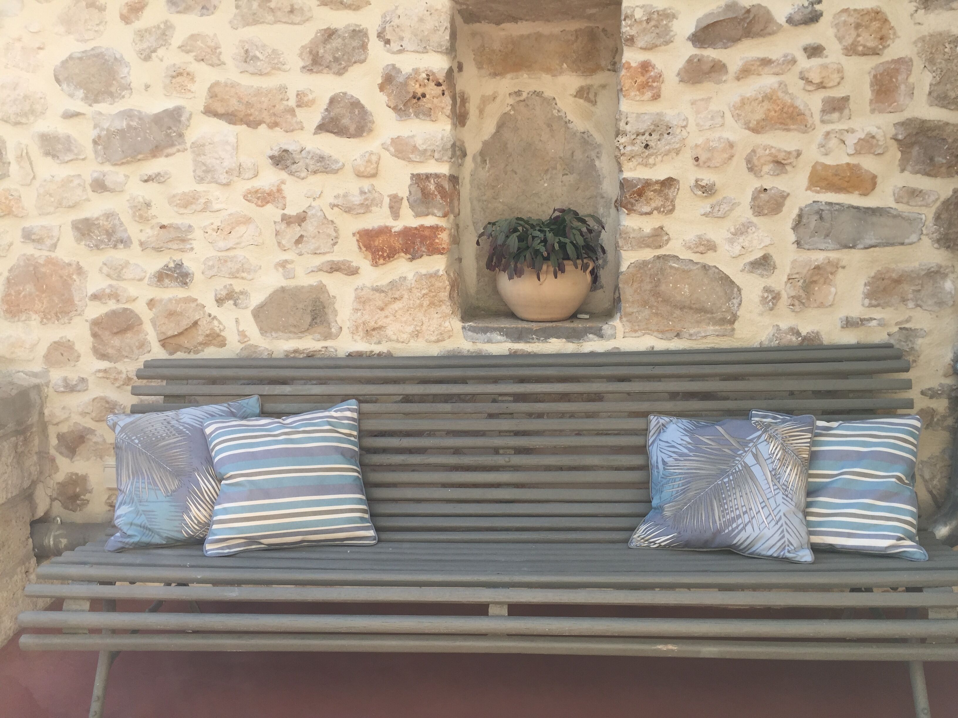 Un muro de piedra con una planta en maceta y un banco con cojines a rayas.