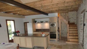 A kitchen with a central island, a dining area with a table and chairs, and a staircase leading to another level. - Former sheepfold in an old village with garden and swimming pool (Saint-Mathieu-De-Tréviers)