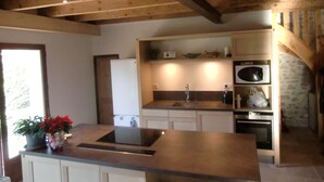A kitchen with wooden beams, a sink, a stove, and a microwave. - Former sheepfold in an old village with garden and swimming pool (Saint-Mathieu-De-Tréviers)
