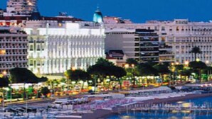 Un paysage urbain côtier avec une plage, des bâtiments et un grand navire de croisière amarré au port.