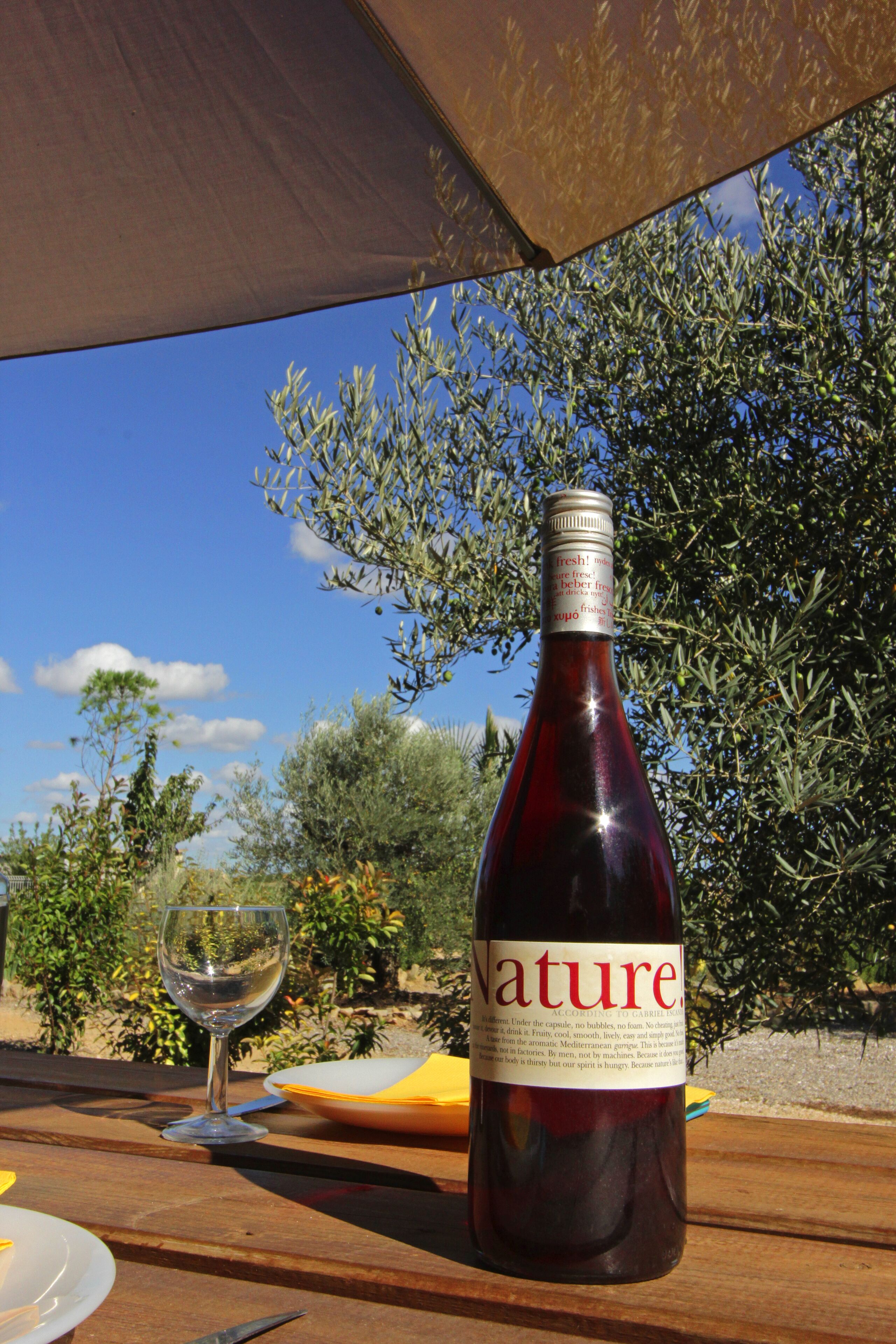 A bottle of wine with a label that reads "Nature" on a wooden table outdoors.