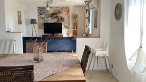 Un coin repas avec une table en bois, des chaises en osier, un téléviseur et une bibliothèque.