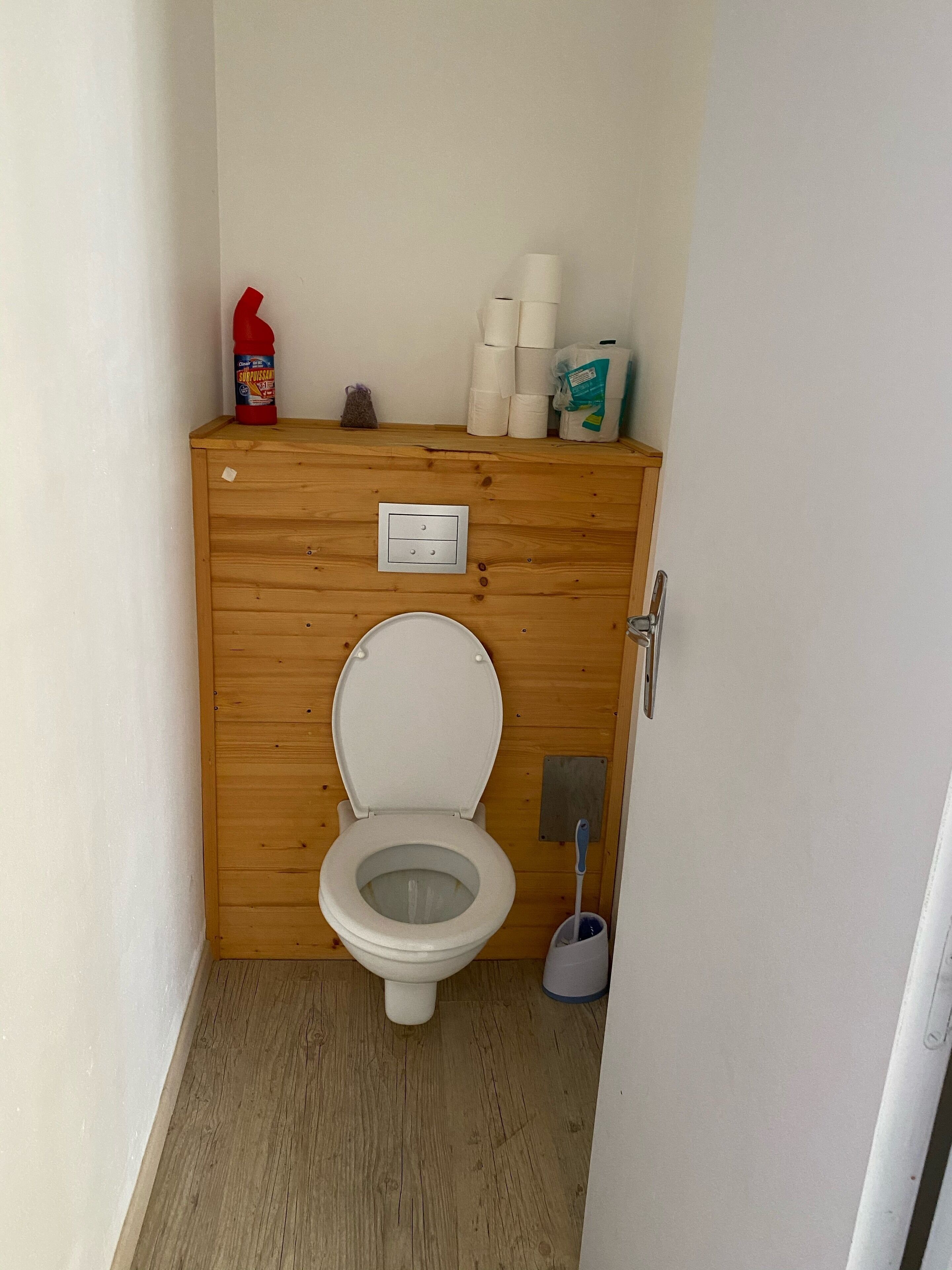 A small, wooden-paneled bathroom with a white toilet, a hand dryer, and toilet paper.